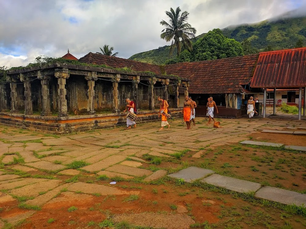 Priests crossing the stone-paved temple courtyard at Thirunelly, the hills behind