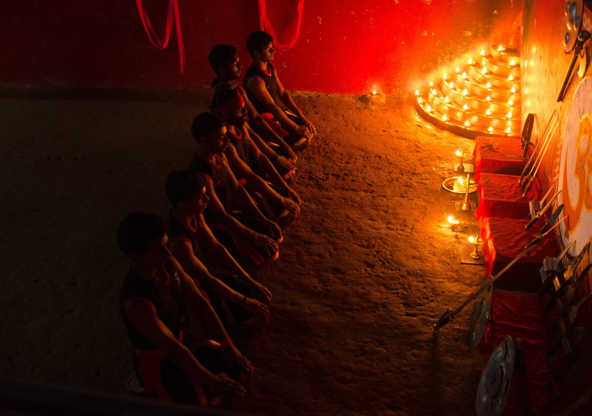 Students saluting in a kalari lit by rows of oil lamps